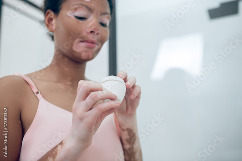 A cute young woman holding a jar of face cream in hands