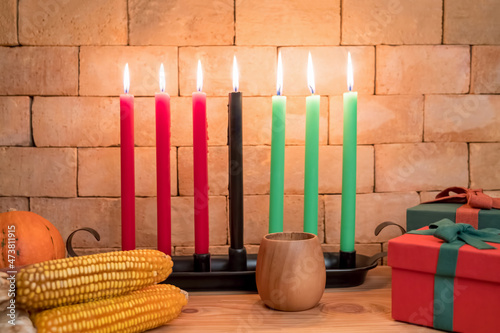 Kwanzaa holiday concept with decorate seven candles red, black and green, gift box, pumpkin,corn and fruit on wooden desk and background. photo