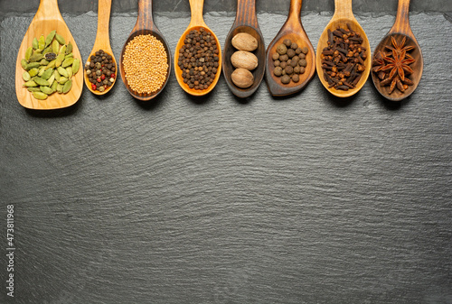 Various herbs and spices in wooden spoons on slate board. Flat lay of spices ingredients pepper, anise star, nutmeg, allspice, clove, mustard seeds and cardamom on slate.