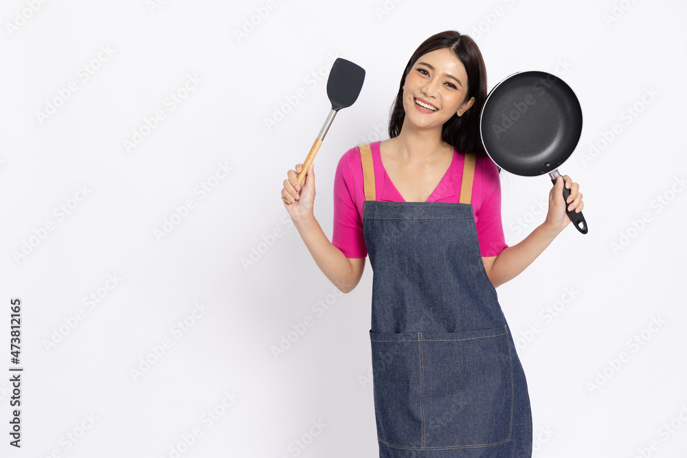 Young Asian woman housewife wearing kitchen apron cooking and holding pan and spatula isolated on white background Young Asian woman housewife wearing kitchen apron cooking and holding pan and spatula isolated on white background