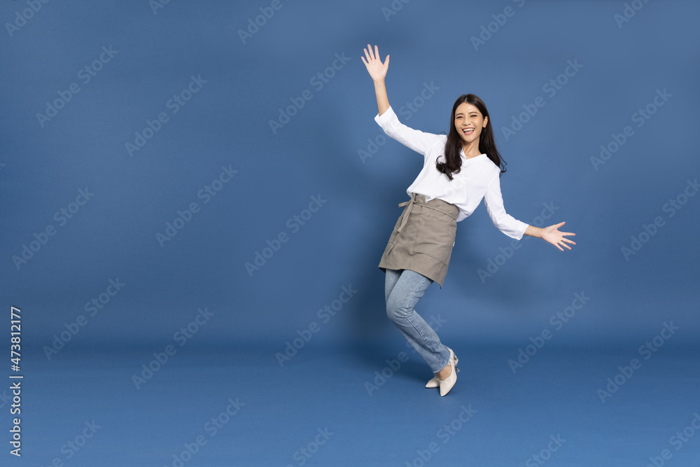 Young Asian woman housewife wearing kitchen apron cooking and dancing isolated on blue background