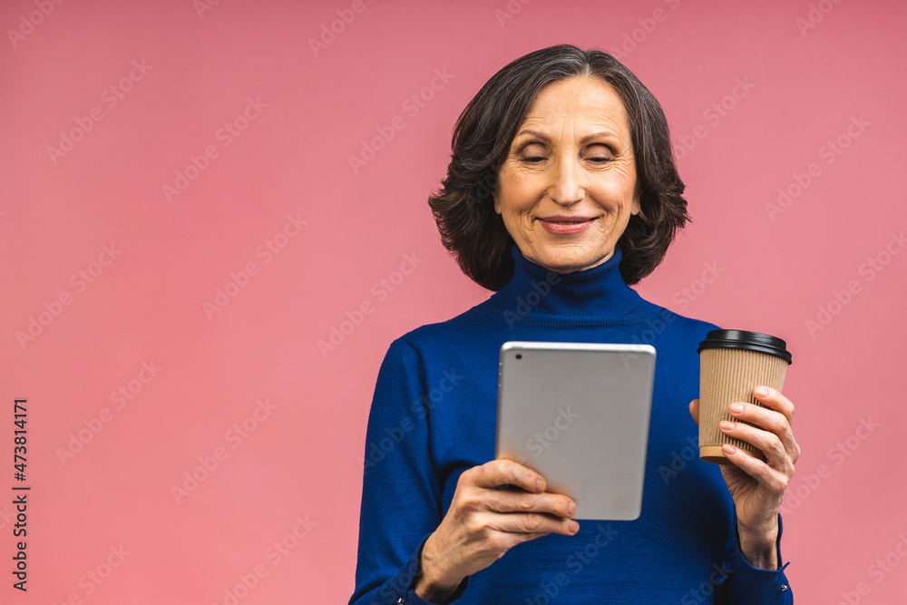 Photo of good mood cheerful smiling senior aged grandmother mature woman drinking coffee isolated on pink color background with copy space for text. Using tablet computer.