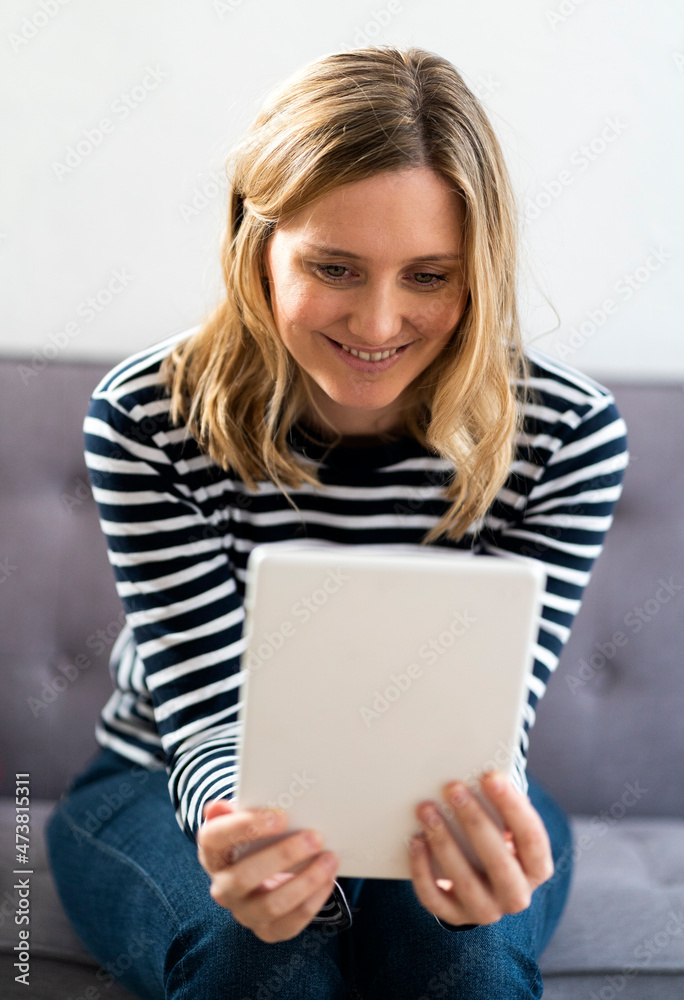 Mid adult woman smiling while using digital tablet at home Mid adult woman smiling while using digital tablet at home