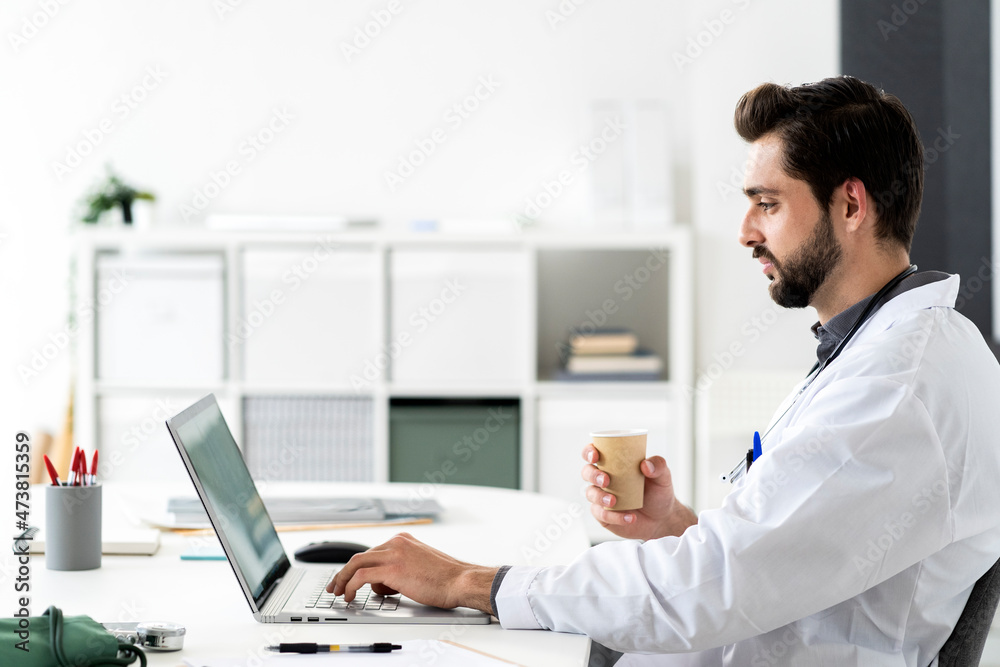 Male doctor using laptop while sitting at desk in hospital Male doctor using laptop while sitting at desk in hospital