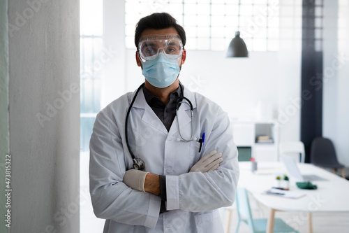 Male healthcare worker wearing protective face standing with arms crossed at hospital photo