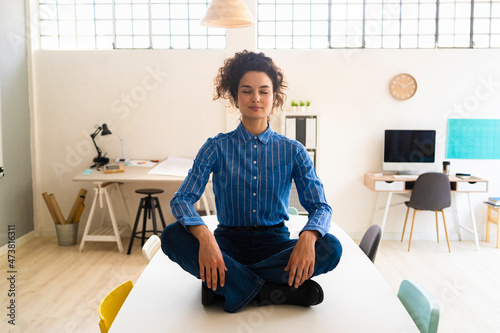 Businesswoman practicing yoga while sitting cross-legged on desk in office