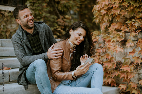 Young couple sitting on outdoor stairs on a autumn day and using mobile phone