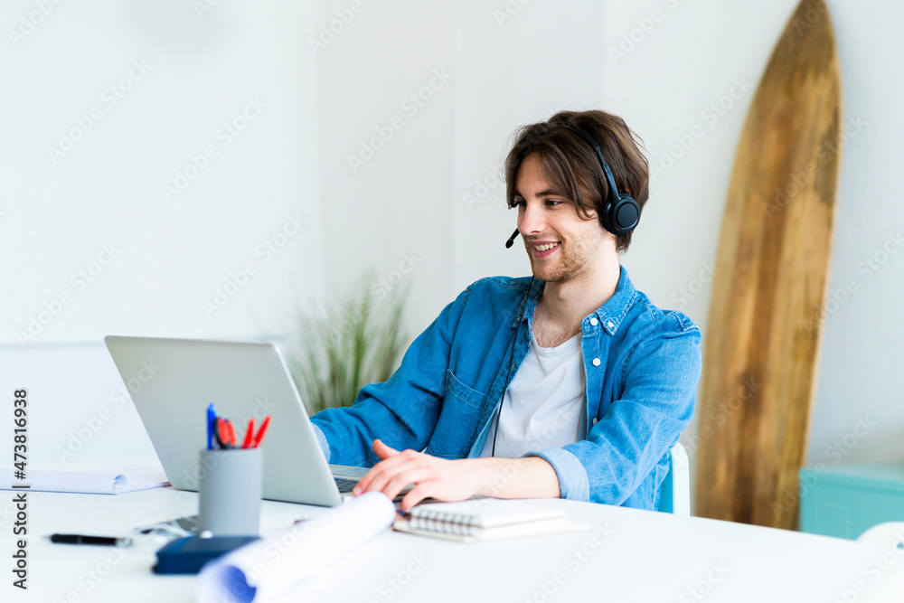 Male entrepreneur with headset using laptop while working in office Male entrepreneur with headset using laptop while working in office