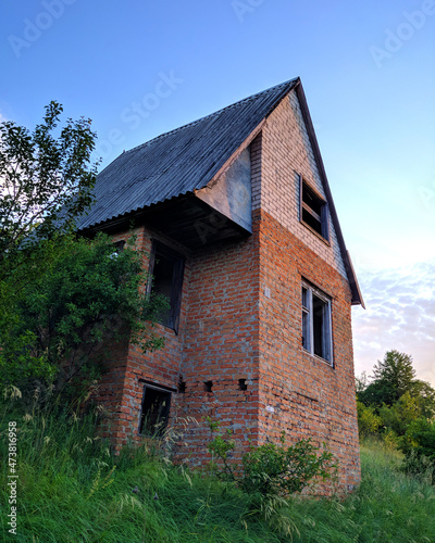Abandoned brick house with a gable slate roof overgrown with greenery