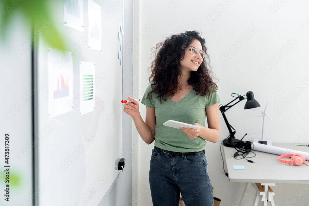 Businesswoman with digital tablet planning business strategy on whiteboard in office Businesswoman with digital tablet planning business strategy on whiteboard in office