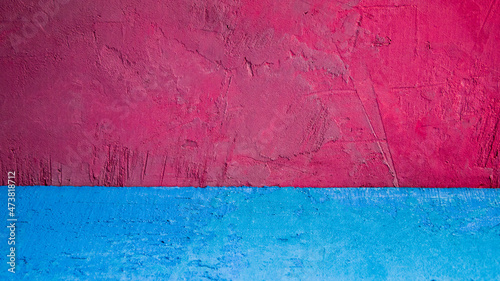 Bright concrete background, which combines rich pink and pale blue. The surface is covered with scratches, cracks and abrasions.