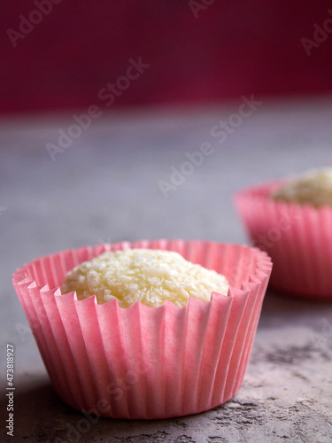 One white coconut candy in a pink wrapper on a gray concrete background. Romantic dessert.