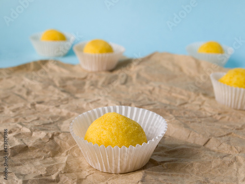Yellow round candies with a taste of citrus in white candy wrappers lie on crumpled brown craft paper. Side view of sweets.