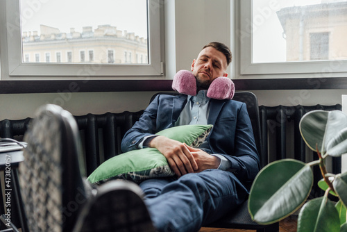 Businessman with neck pillow relaxing on chair in office photo