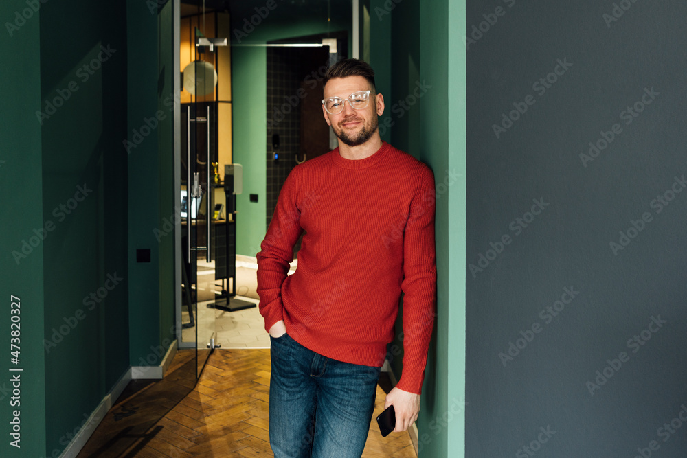 Smiling businessman with hand in pocket leaning on wall at workplace Smiling businessman with hand in pocket leaning on wall at workplace