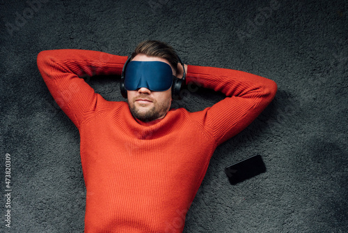 Male professional napping with eye mask while listening music through headphones at workplace photo