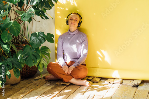 Woman listening music through headphones in front of yellow backdrop photo