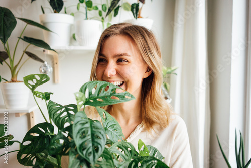 Happy blond woman looking away while standing behind plant at home