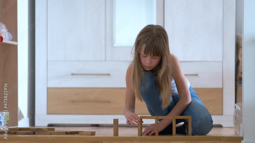 Creative child girl playing with game stacking wooden toy blocks in high building structure. Hand movement control and concentration skills concept Creative child girl playing with game stacking wooden toy blocks in high building structure. Hand movement control and concentration skills concept