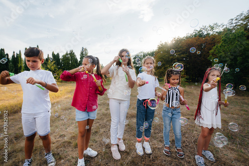 A large group of cheerful children play in the Park and inflate soap bubbles. Games in a children's camp