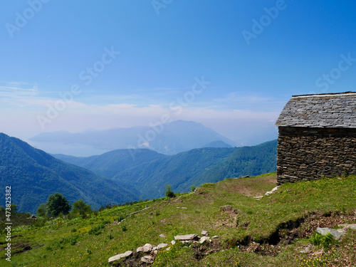 Traditional stone hut at Cima Sasso in Val Grande, national park in Piedmont, Italy. Panoramic view of Lago Maggiore.