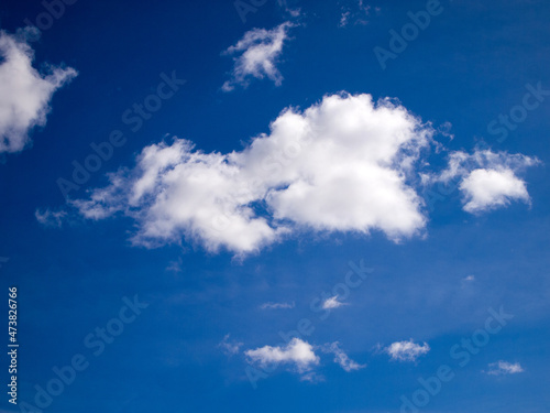 White clouds on a saturated blue sky on a bright sunny day. Natural background. View from the ground.