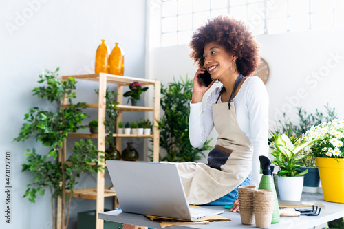 Female florist talking on mobile phone while sitting by laptop on table photo