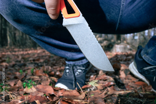 A sharp knife in a man's hand. A man sits in the woods with a knife in his hand