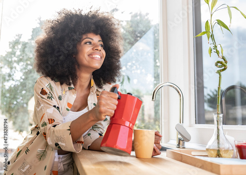 Afro woman pouring coffee from kettle in mug on kitchen counter at home photo