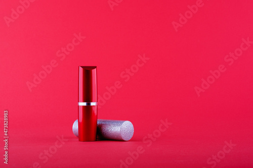 two bottles of lipstick grey lies red standing on a red background