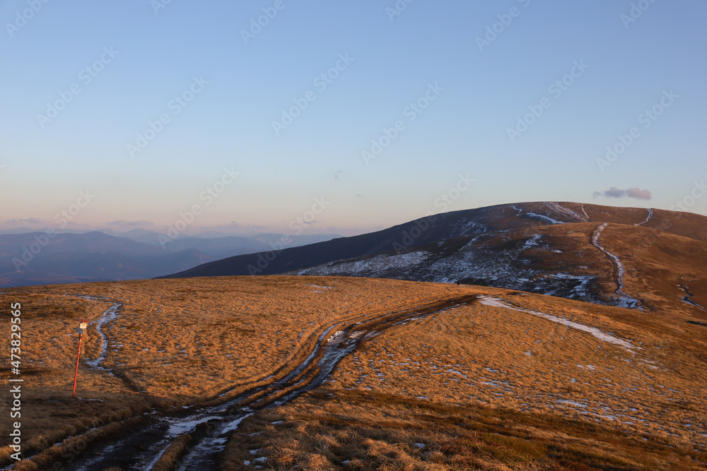 Autumn landscape in the Carpathian mountains. Dirt road with snow on the Borzhava ridge. Sunset lighting