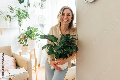 Happy woman holding plant while leaning on wall in living room