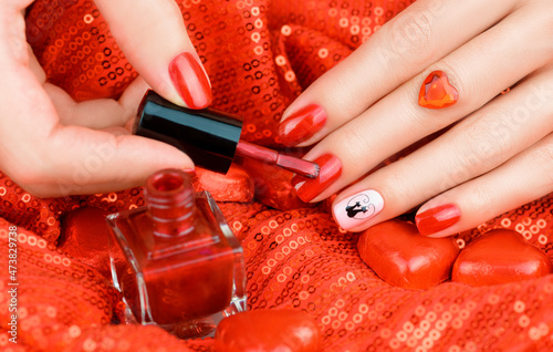 Bright red manicure. Woman paints her nails with red varnish. Festive manicure for Valentine's Day.