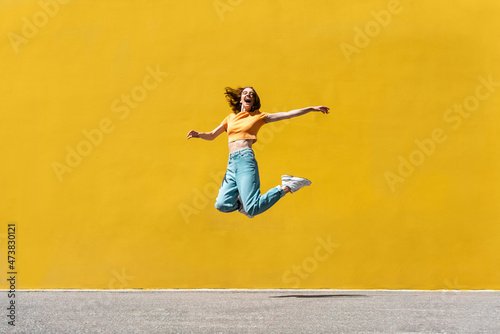 Cheerful woman with arms outstretched jumping on footpath