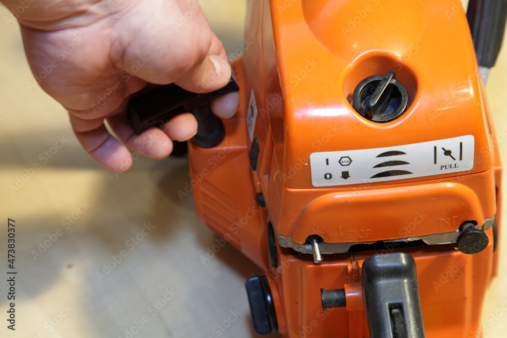 A man's hand starts a chainsaw engine with a manual starter closeup