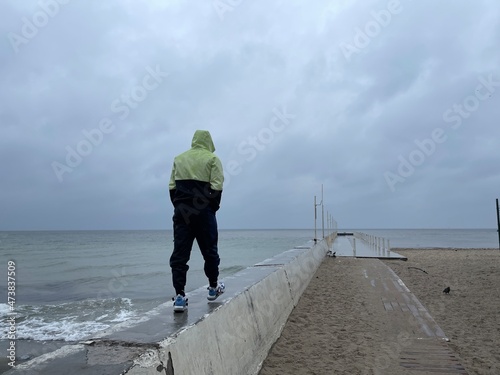 Fotografie Rear view shot of a man walking on concrete pier under the rain