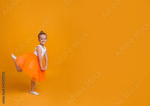 Cute little girl in tutu skirt dancing on orange background. space for text