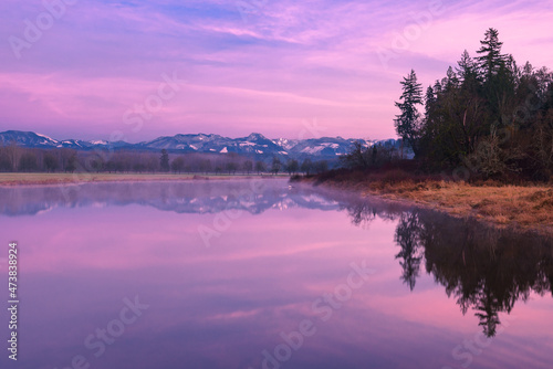 A purple and blue sunset illuminates a smooth lake and distant mountains on the horizon. The tranquil scene is in the Snoqualmie Valley of Washington State