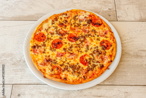 Cannibal Pizza with Bacon, Ground Beef, Pepperoni Slices and Lots of Mozzarella Cheese on a Round White Porcelain Plate