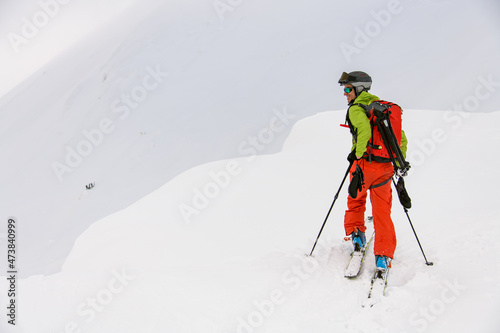rear view of man skier with trekking poles walking along snowy mountain slope