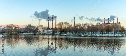 Smoking chimneys of thermal power plants near the waterfront in city. Winter. Industrial and nature background.