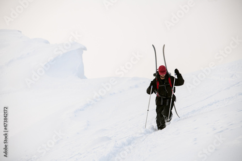 man with trekking poles walks through deep powdery snow on a mountain slope
