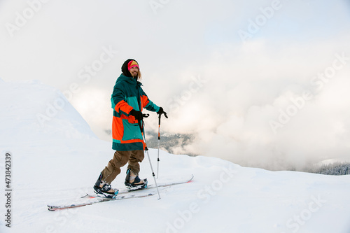 Man freerider in colorful suit with skis near snow-covered mountain slope