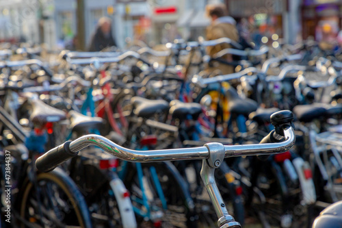 Selective focus of bicycle handlebar in bike storage, Outdoor parking area along street with blurred view of peoples, Netherlands land of bicycles, Cycling is a common mode of transport in Holland.