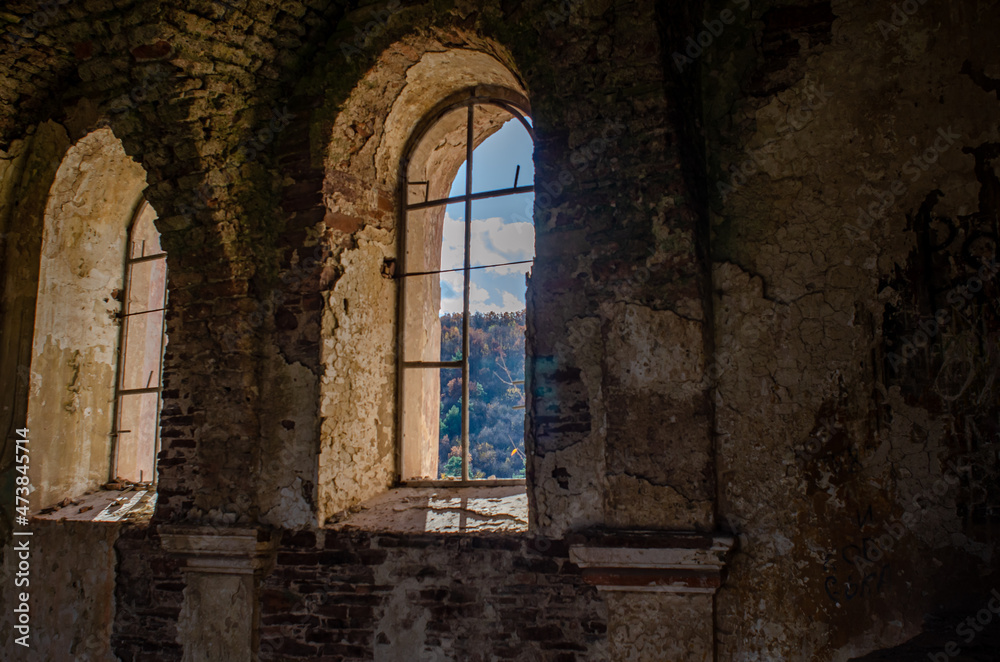 View of  forest under blue sky through windows of old ruined church.