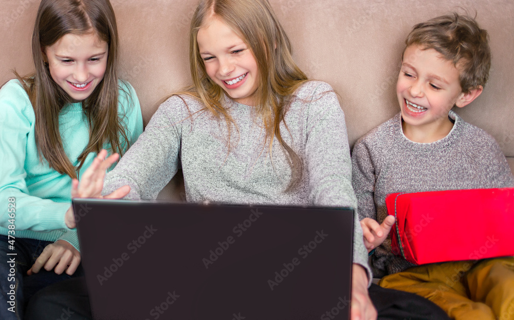 Two girls and a boy are sitting in front of a laptop. They smile, wave their hands and communicate. Online holiday concept