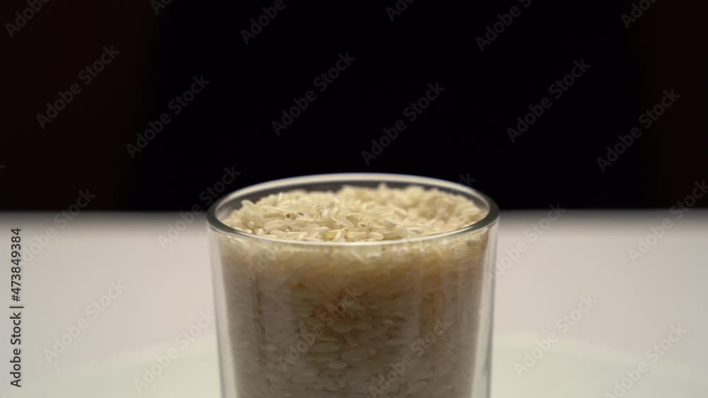 A man's hand picks up white rice with a teaspoon from a glass. Recipes with white rice. The benefits of white rice for the organism. Rice is the main food of long-livers. Culture of Eastern countries. A man's hand picks up white rice with a teaspoon from a glass. Recipes with white rice. The benefits of white rice for the organism. Rice is the main food of long-livers. Culture of Eastern countries.