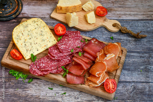 Italian dried thinly sliced artisan pork salami Milano , parmesan cheese, tomatoes and fresh basil on wooden background .Rustic home made italian snack.
