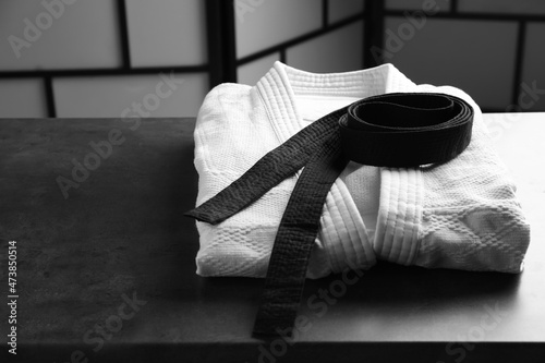 Martial arts uniform with black belt on grey stone table indoors