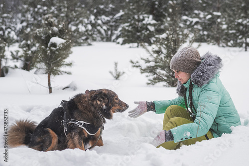 Woman having fun with dog in the snow in forest